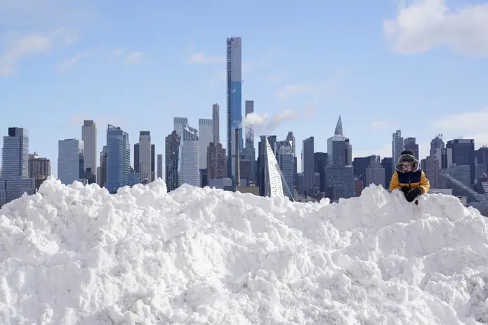 Boy plays on a mound of snow in front of the skyline.